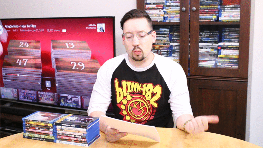 Tim Kuefler presenting at a table with blu rays, mid-prep on a pop culture and creative theory video